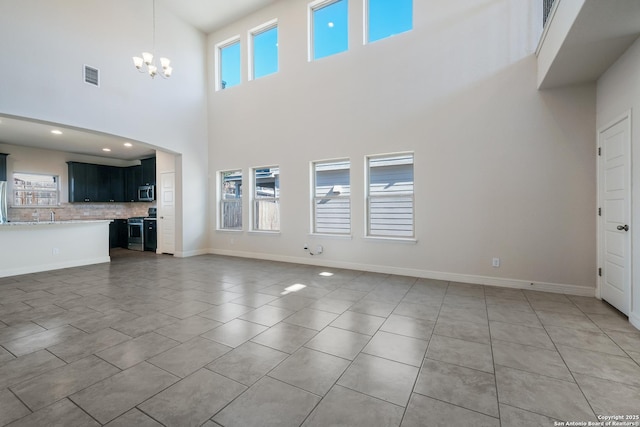 unfurnished living room with a notable chandelier, a towering ceiling, plenty of natural light, and tile patterned floors