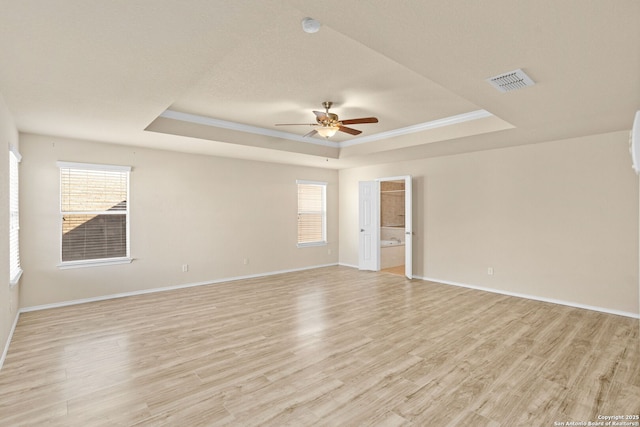 empty room with ceiling fan, ornamental molding, light wood-type flooring, and a tray ceiling