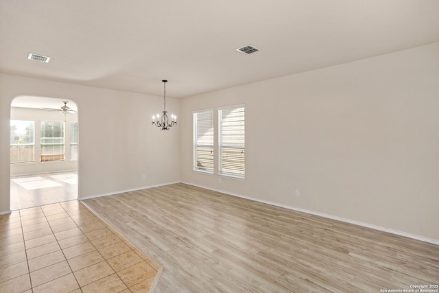 unfurnished room featuring a healthy amount of sunlight, ceiling fan with notable chandelier, and light hardwood / wood-style flooring