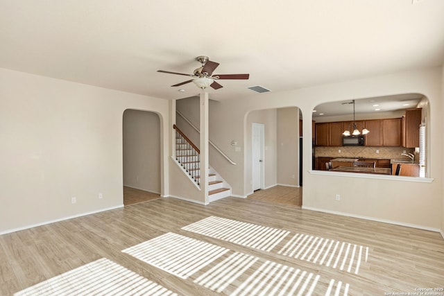 unfurnished living room featuring sink, ceiling fan with notable chandelier, and light hardwood / wood-style flooring