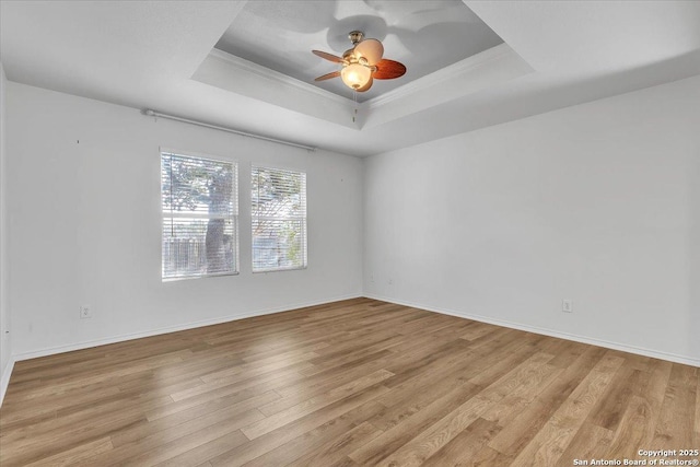 spare room with a tray ceiling, light hardwood / wood-style flooring, ornamental molding, and ceiling fan