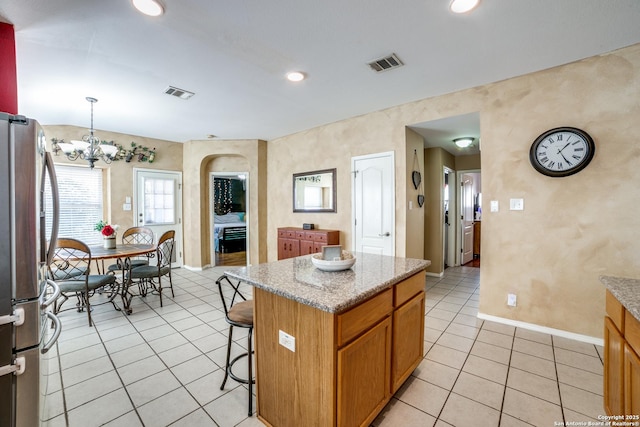 kitchen with a kitchen island, stainless steel fridge, hanging light fixtures, light tile patterned floors, and a notable chandelier