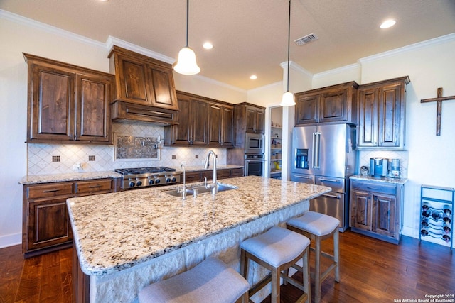 kitchen featuring pendant lighting, sink, stainless steel appliances, and an island with sink