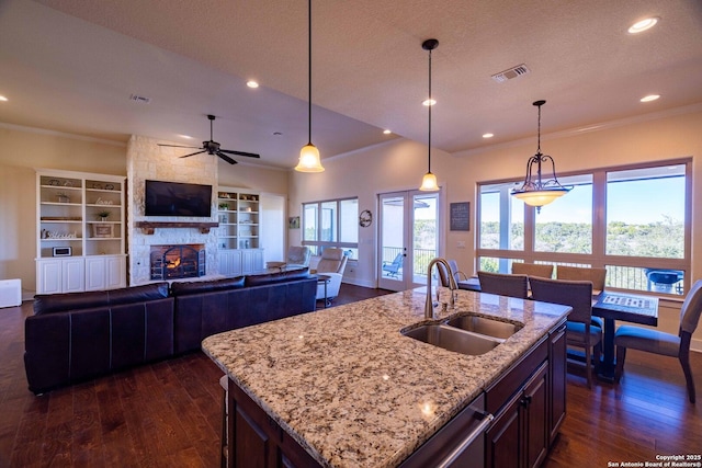 kitchen featuring pendant lighting, a fireplace, sink, a kitchen island with sink, and light stone countertops