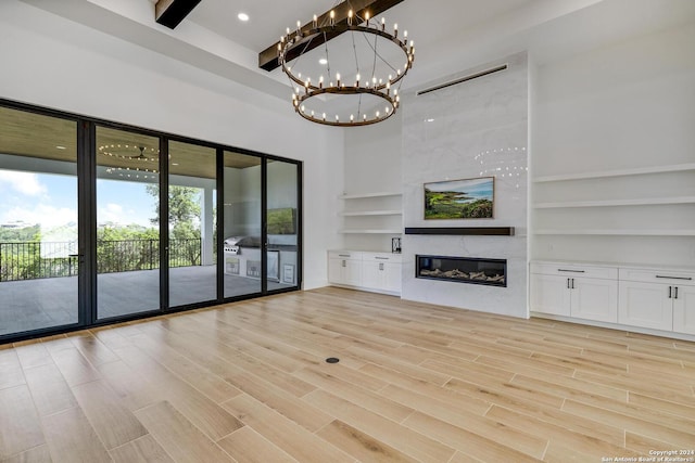 unfurnished living room featuring a towering ceiling, beamed ceiling, a chandelier, light hardwood / wood-style floors, and a premium fireplace