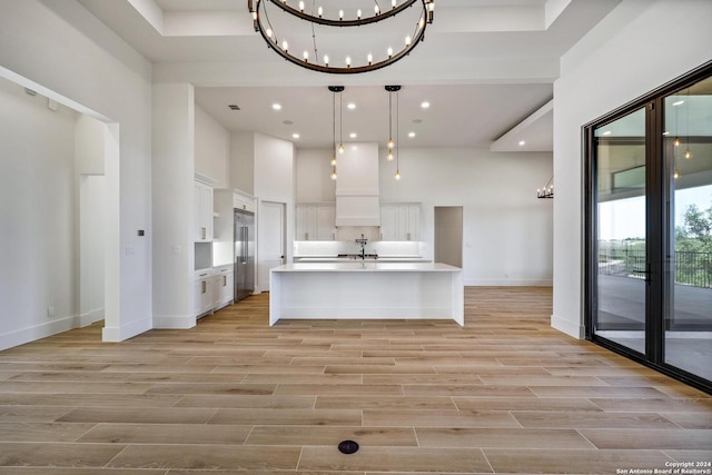 kitchen featuring built in refrigerator, a kitchen island with sink, hanging light fixtures, backsplash, and white cabinets