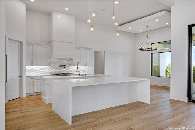 kitchen featuring a large island with sink, hanging light fixtures, white cabinets, and backsplash