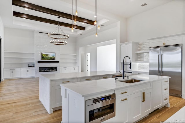 kitchen featuring white cabinetry, a kitchen island with sink, sink, and stainless steel built in fridge