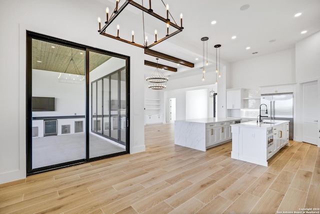 kitchen featuring pendant lighting, stainless steel built in refrigerator, an island with sink, white cabinets, and beamed ceiling