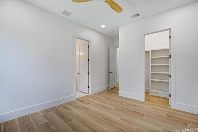 unfurnished bedroom featuring a spacious closet, light hardwood / wood-style floors, a closet, and ceiling fan