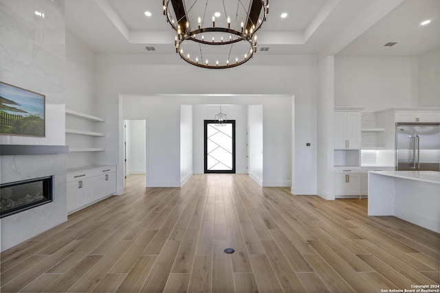 unfurnished living room with a towering ceiling, a high end fireplace, and light hardwood / wood-style floors