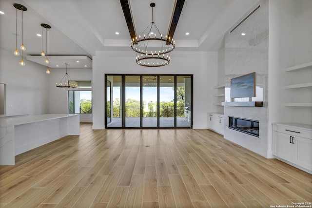 unfurnished living room featuring light hardwood / wood-style flooring, built in shelves, a high end fireplace, and a high ceiling