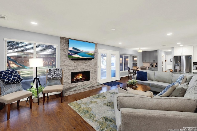 living room with a stone fireplace, dark hardwood / wood-style flooring, and french doors