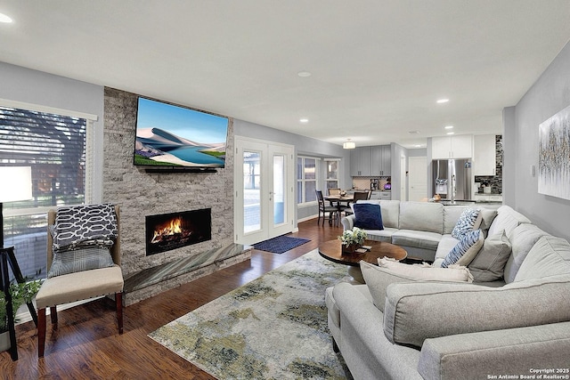 living room featuring a stone fireplace, dark wood-type flooring, and french doors