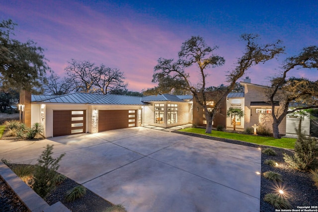 modern home featuring a garage, concrete driveway, a chimney, metal roof, and a standing seam roof