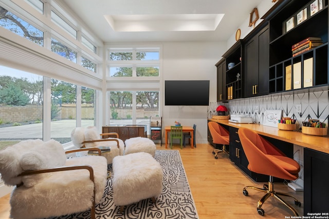 interior space featuring light wood-style flooring, a high ceiling, a raised ceiling, and built in study area