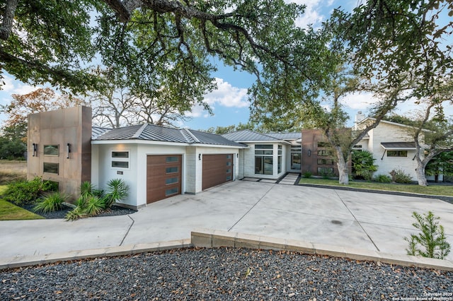 modern home featuring a garage, metal roof, driveway, and a standing seam roof