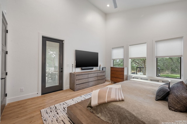 bedroom featuring access to exterior, recessed lighting, light wood-style flooring, a towering ceiling, and baseboards