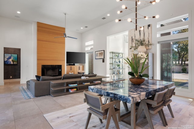 dining room featuring recessed lighting, a fireplace, visible vents, a towering ceiling, and an inviting chandelier