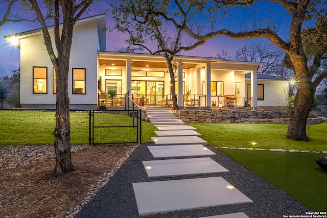 back of house at dusk featuring a yard, covered porch, and stucco siding