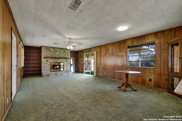 unfurnished living room with a stone fireplace, carpet floors, ceiling fan, and wood walls