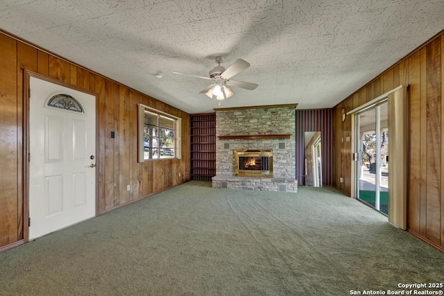 unfurnished living room with ceiling fan, carpet, wooden walls, and a fireplace