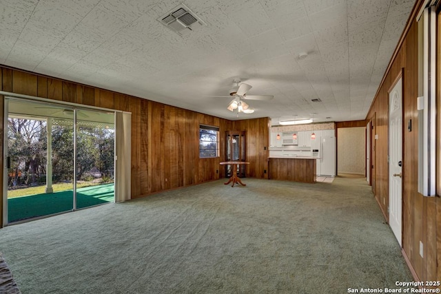 unfurnished living room with ceiling fan, wooden walls, and light carpet