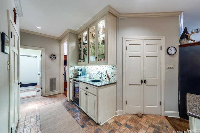 kitchen featuring wine cooler, sink, crown molding, dark stone countertops, and decorative backsplash