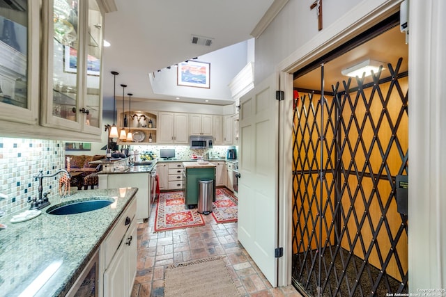 kitchen with sink, hanging light fixtures, ornamental molding, light stone countertops, and decorative backsplash