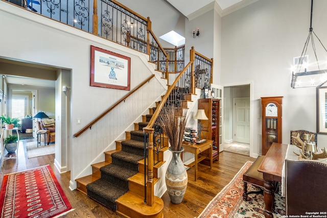 staircase with wood-type flooring, a towering ceiling, and ornamental molding