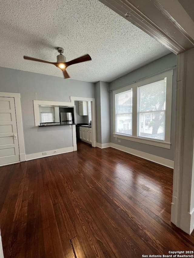 unfurnished living room with ceiling fan, dark hardwood / wood-style flooring, and a textured ceiling