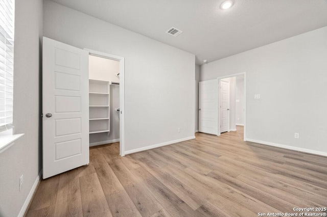 unfurnished bedroom featuring a walk in closet, a closet, and light wood-type flooring