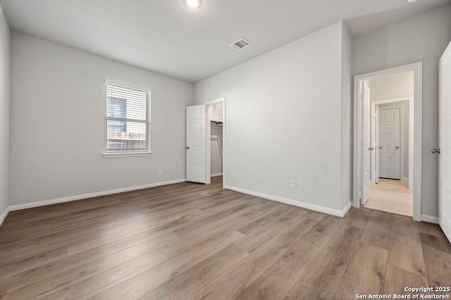 unfurnished bedroom featuring a walk in closet, a closet, and light wood-type flooring