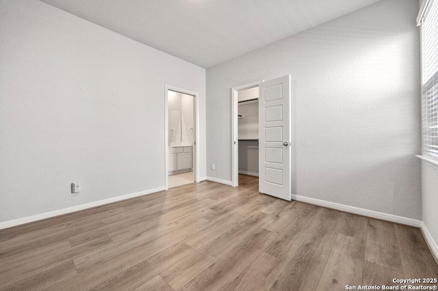 unfurnished bedroom featuring ensuite bath, a walk in closet, light hardwood / wood-style floors, and a closet