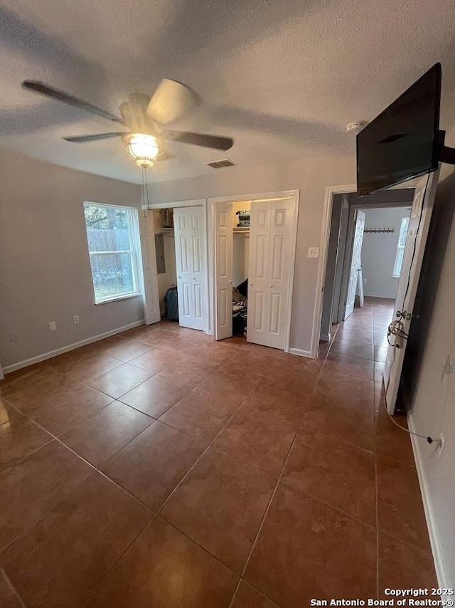 unfurnished bedroom featuring dark tile patterned flooring, a textured ceiling, and ceiling fan