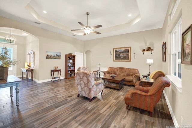 living room featuring a tray ceiling and ceiling fan with notable chandelier