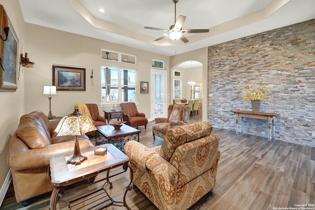 living room with a raised ceiling, wood-type flooring, and ceiling fan