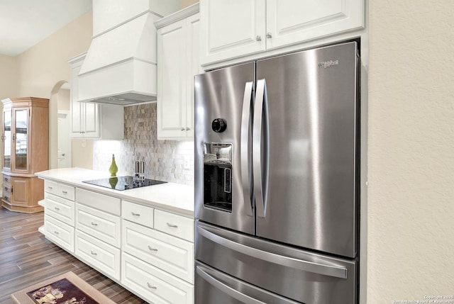 kitchen featuring custom exhaust hood, black electric cooktop, stainless steel fridge, white cabinets, and backsplash