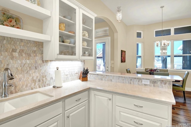 kitchen with white cabinetry, hanging light fixtures, backsplash, and sink