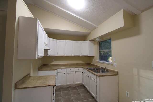 kitchen with sink, dark tile patterned floors, white cabinetry, a textured ceiling, and vaulted ceiling