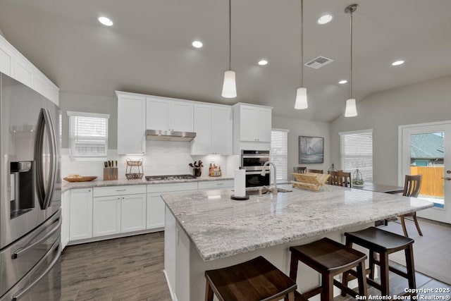 kitchen with an island with sink, appliances with stainless steel finishes, and decorative light fixtures