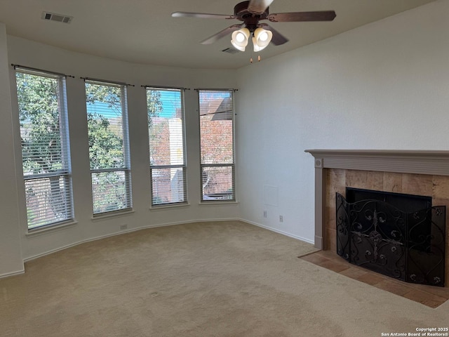 unfurnished living room featuring a tiled fireplace, light colored carpet, and ceiling fan