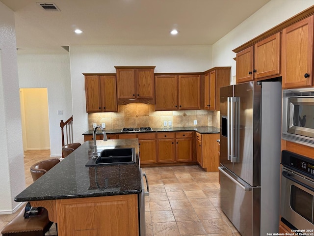 kitchen featuring sink, appliances with stainless steel finishes, dark stone countertops, an island with sink, and a kitchen bar