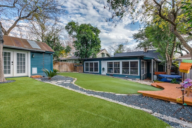 back of property with french doors, a sunroom, a wooden deck, and a lawn