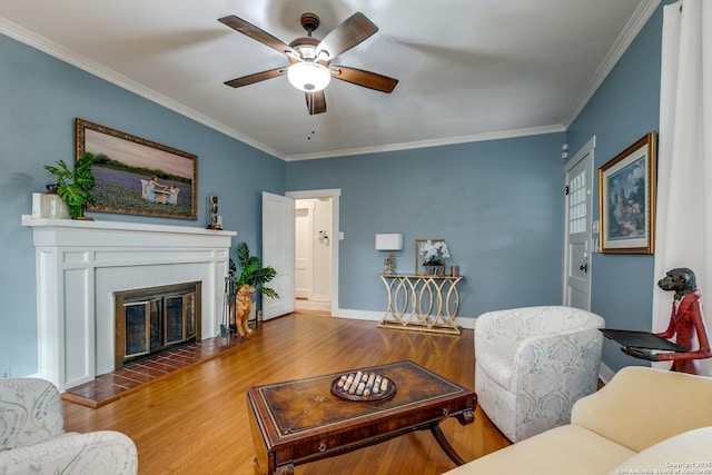 living room featuring ceiling fan, ornamental molding, a tiled fireplace, and hardwood / wood-style floors