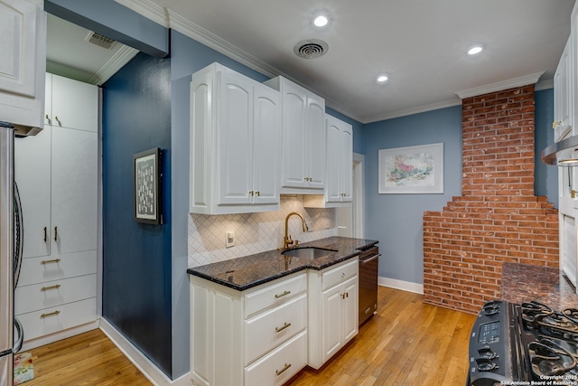 kitchen with sink, dark stone countertops, ornamental molding, white cabinets, and light wood-type flooring