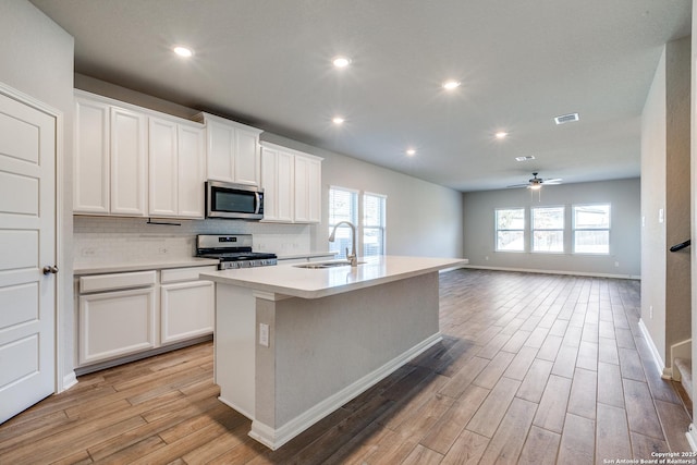 kitchen with white cabinetry, a center island with sink, light hardwood / wood-style flooring, stainless steel appliances, and decorative backsplash