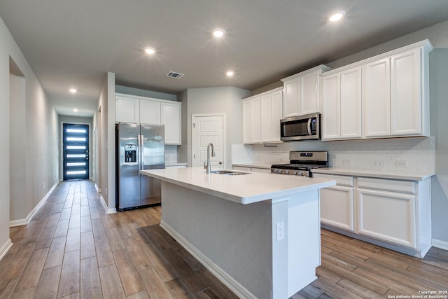 kitchen featuring stainless steel appliances, an island with sink, sink, and white cabinets