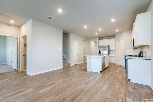 kitchen featuring tasteful backsplash, white cabinets, a kitchen island with sink, stainless steel appliances, and light hardwood / wood-style flooring