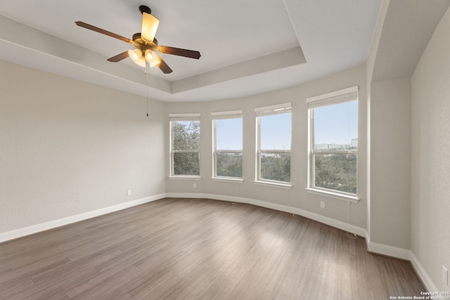 spare room with ceiling fan, a tray ceiling, and light wood-type flooring